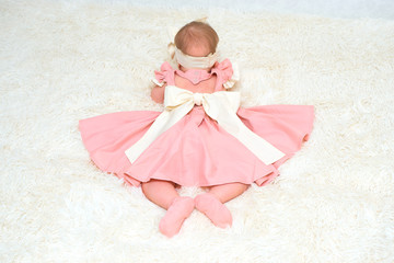 A little girl in a beautiful dress is lying on a blanket