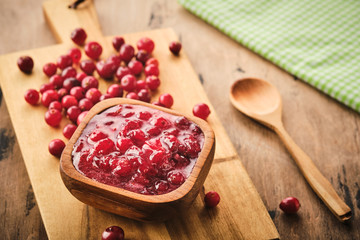 Cranberry jam in a wooden bowl on a wooden background.