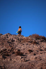 Fototapeta na wymiar Teenage boy running a rocky mountain trail uphill against blue sky