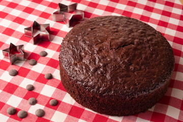 Chocolate sponge cake on a red and white tablecloth with pieces of chocolate and stars
