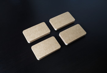 Four piles of blank kraft business cards on black wooden background. Corporate ID template.