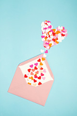 Pink envelope with heart shaped confetti over the blue background. Love, letter, message, saint valentines day concept