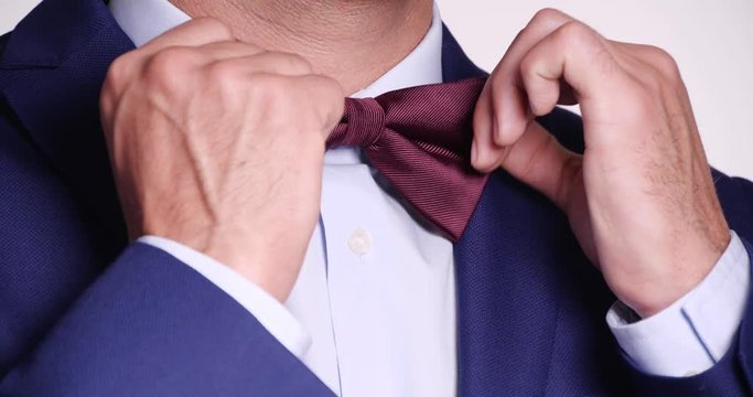 Man in elegant suit adjusting bow tie on white background, closeup