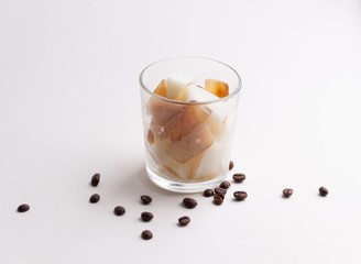glass of frozen ice coffee and milk pieces on white background with coffee beans