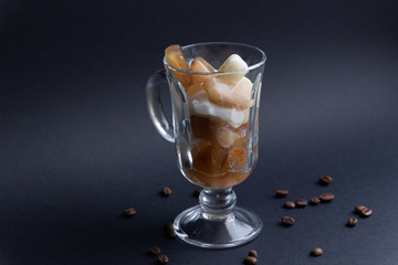 glass of melting frozen ice coffee and milk pieces on black background with coffee beans
