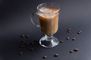 glass cup of melting frozen ice in coffee and milk on black background with coffee beans