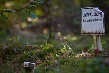 A sign in German with the inscription: Investigation of forest and groundwater and a well cover in the forest with moss and trees