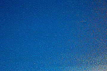 water drops on a glass pane with reflections and a blue background