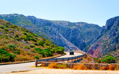 Naklejka premium Car on the road at Buggerru in Sardinia Island in Italy summer. Transport driving on the highway of Europe. Holiday View on motorway. Cagliari province. Mountains on background. Mixed media.