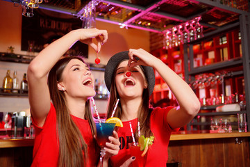 Two young girls lesbians at a party in the club are holding cocktail cherries.