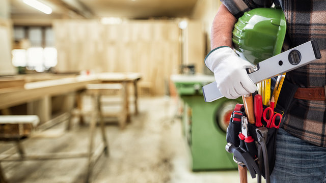 Close-up. Carpenter with hands protected by gloves holds helmet and level. Construction industry, carpentry workshop.