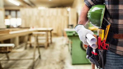 Close-up. Carpenter with his hands protected by gloves holds the helmet and the project. Construction industry, carpentry workshop.