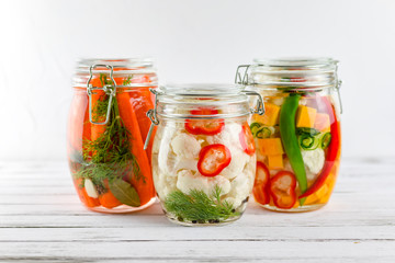 three glass jars of fermented cauliflower,carrots,chili pepper, vegetables on a light background. fermentation is a source of probiotic