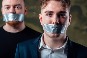two young man with mouth and lips sealed covered with grey adhesive tape in censorship coerced...