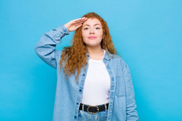 young red head woman greeting the camera with a military salute in an act of honor and patriotism,...