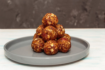 Homemade energy balls like a healthy breakfast or a snack of raisins, dried apricots, dates, nuts and oatmeal, thet lie on  a gray ceramic plate on a white wood background. Horizontal orientation.