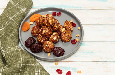 Homemade energy balls like a healthy breakfast or a snack of raisins, dried apricots, dates, nuts and oatmeal, that lie on  a gray ceramic plate on a white wood background and green towel. 