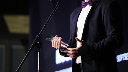 Middle shot of business man winner holding a glass statue prize enjoying a victory and making grateful speech on stage performance. Award ceremony.