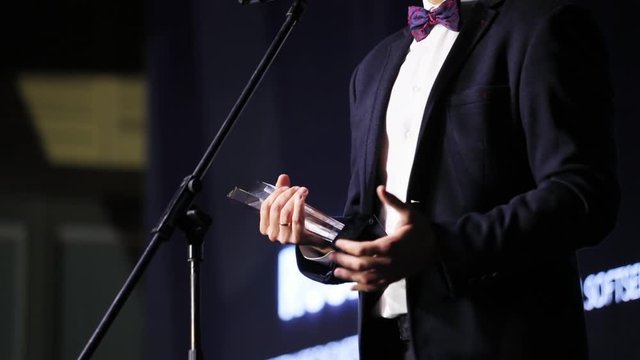 Middle shot of business man winner holding a glass statue prize enjoying a victory and making grateful speech on stage performance. Award ceremony.