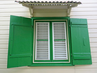 White wooden window, green shutters and sheet roof on the exterior of a white house. Vintage green window shutters. Caribbean architecture - Powered by Adobe