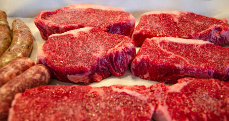 New York Strip steaks on a board with salt and pepper.  Raw sausages. Barbecue.