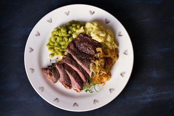 Grilled fillet beef steak with mashed potato, peas and fried onion. View from above, top view