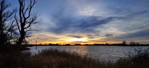 A fantastic sunset with red yellow orange and purple tones with dramatic cloud formation over the Baltic Sea with bare trees and reeds