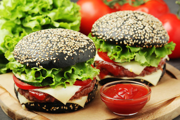 Two black burgers with vegetables and beef meat	