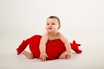 baby boy 9 months old smiling and holding a red pillow in the shape of a heart, sitting on a white background, isolate, space for text.concept of Valentine's day