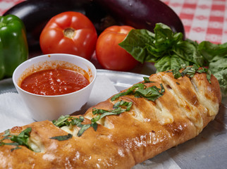 Freshly baked Stromboli on the table setting fresh basil, green peppers and tomato sauce
