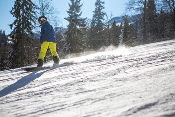 A beautiful sunny day on the mountain, the snowboarder goes down the slope, wearing a blue jacket...
