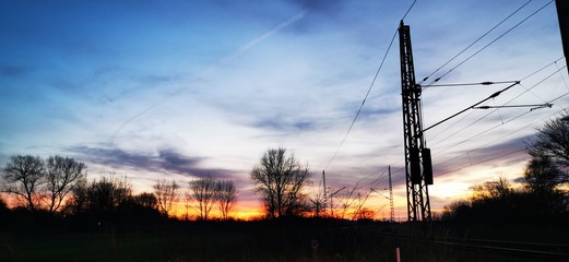A fantastic sunset with red yellow orange and purple tones with dramatic cloud formation over green meadows with bare trees in January on the island of R&uuml;gen