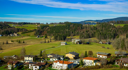 Fototapeta na wymiar aerial landscape top view of European village country side Austrian outskirts landmark houses on highland spring time valley with green grass and trees foliage with horizon background line blue sky