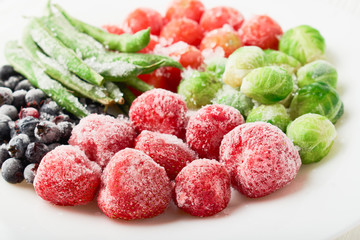 White plate with frozen food in a plate - strawberries with shadberry and brussels sprouts with...