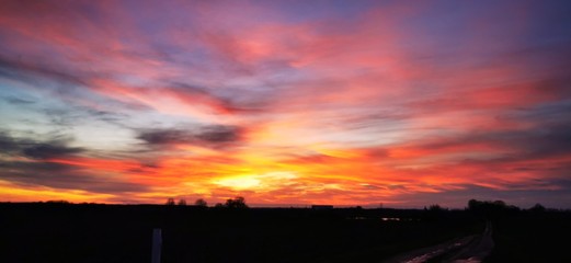 A fantastic sunset with red yellow orange and purple tones with dramatic cloud formation over green meadows with bare trees in January on the island of R&uuml;gen