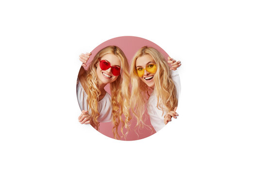 Portrait of two young happy, shocked women in the heart shape sunglasses looking throth the white hole in the wall. Big sale. Funny faces. Empty space for text