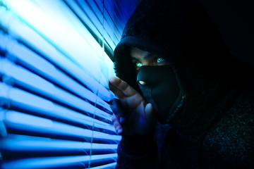 Criminal robber is spying through the window. Old shutter blinds.