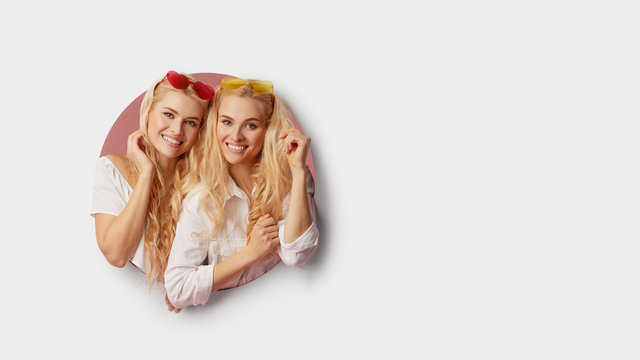 Portrait of two young happy, shocked women in the heart shape sunglasses looking throth the white hole in the wall. Big sale. Funny faces. Empty space for text