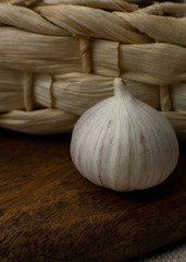 One solo garlic near wicker basket on wooden table close-up macro