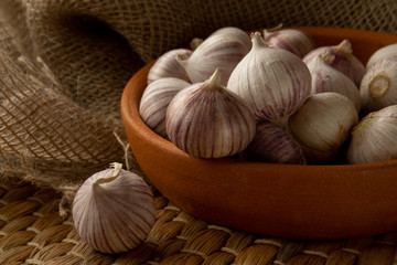 Solo garlic in clay plate on straw mat and textile, view from above