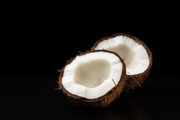 Coconut on a black background. Two halves of a nut. Coconut chopped in half. White flesh.