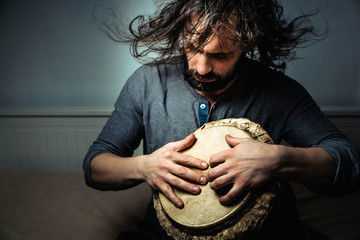 Long-haired man playing an ethnic percussion musical instrument jembe. Drummer playing african music
