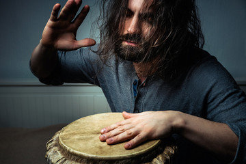 Long-haired man playing an ethnic percussion musical instrument jembe. Drummer playing african music