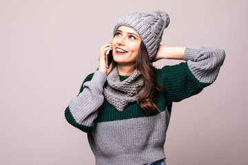 Happy young woman in knit winter clothing making phone call isolated on gray