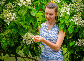 Environmental portrait of beautiful young woman enjoying white flowers in garden