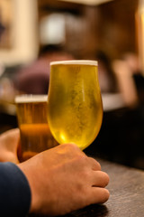 Hands holding misty glasses with two pints of cold Scotch ale, pale ale, lager draft beer in English pub