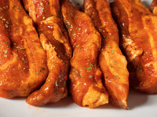 Korean style marinated pork belly slices, close up, on a white plate. Fresh meat preparation.