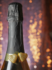 Two golden hearts covered with glitter on a champagne or sparking wine neck, Blurred bokeh background. Saint Valentine theme.