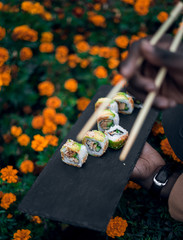 man hold sushi on black stone board on yellow flowers background