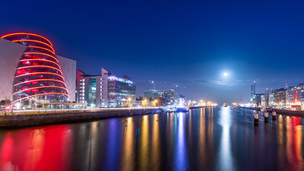 Naklejka premium Niebieska godzina w dokach w Dublinie, widok na centrum kongresowe i rzekę Liffey. Pięknie oświetlony nabrzeże i port w pełni księżyca. Irlandia